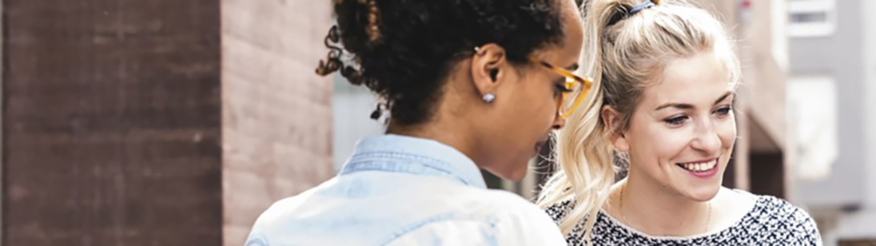  Två glada kvinnor står och tittar på något tillsammans. Kanske letar de svar på vår webbplats.