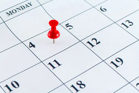 Ett månadsuppslag i en kalender där en dag är markerat med ett rött stift.