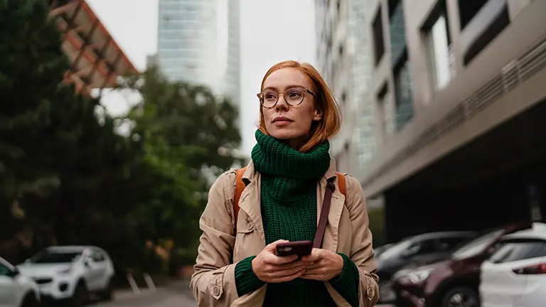 En kvinna framför ett höghus och en mobil i handen.