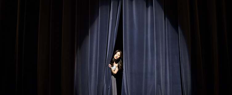 En kvinna kikar fram i ridån på en scen.