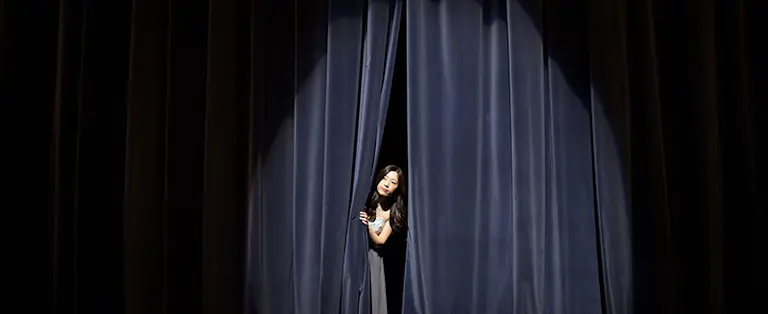 En kvinna kikar fram i ridån på en scen.